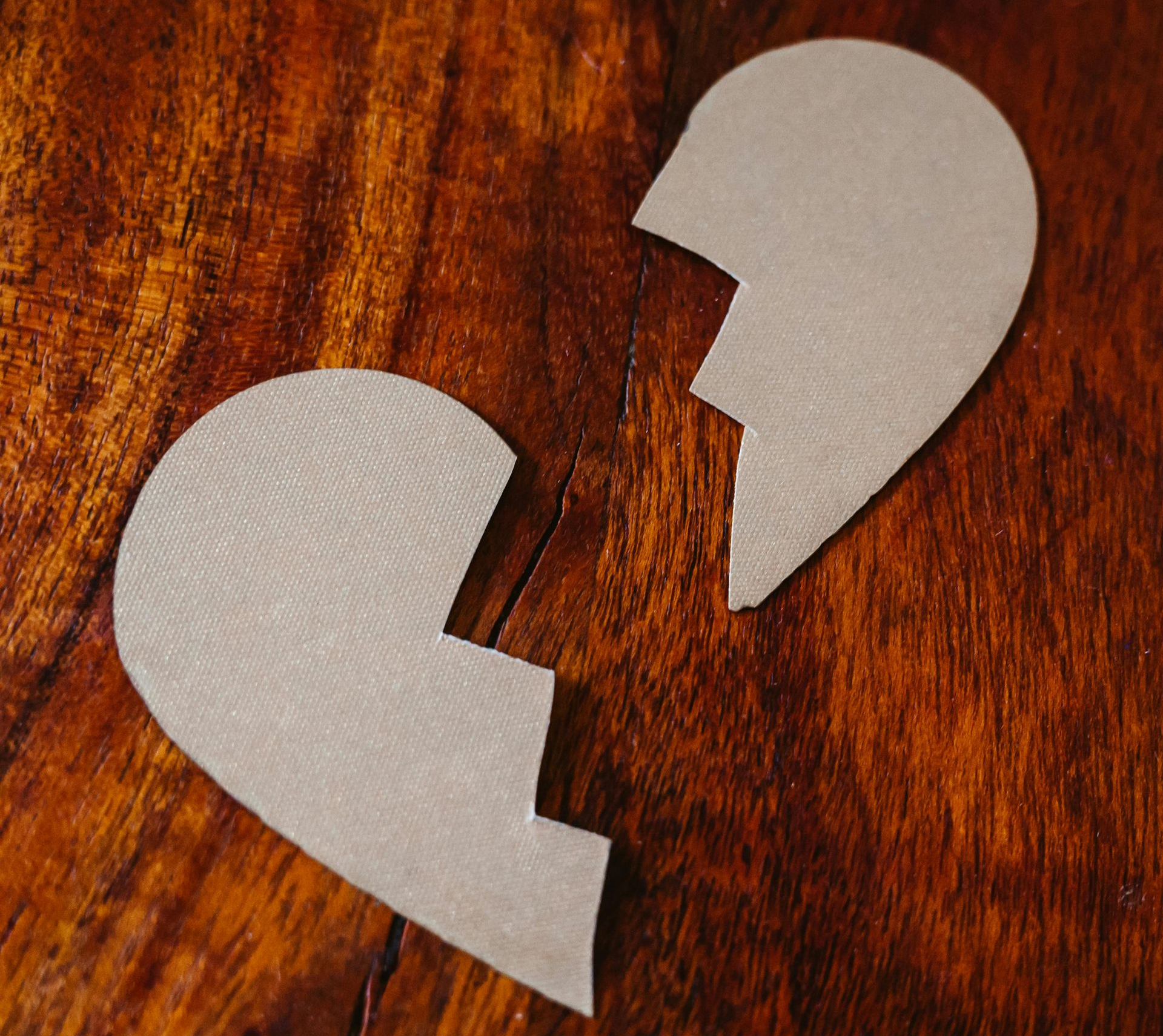 Two cardboard pieces shaped like a broken heart on a wooden surface.